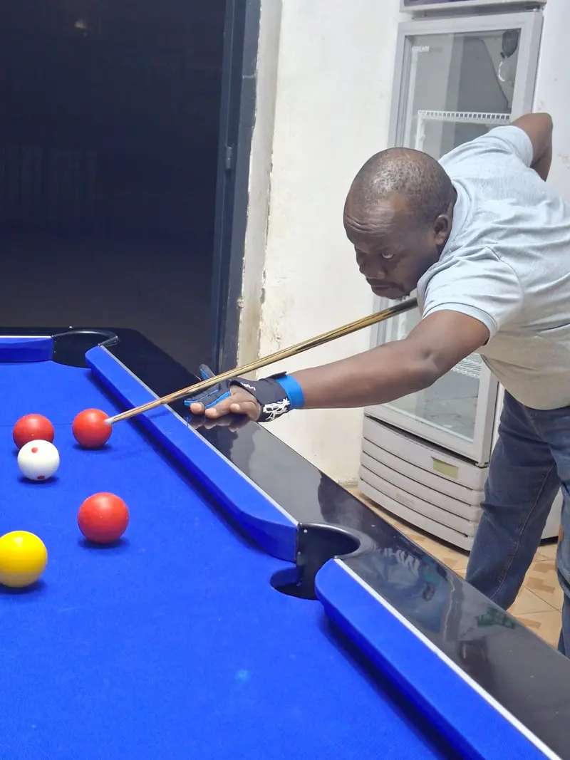 A player in a grey shirt and bridge glove cues up on a red ball on a blue pool table.